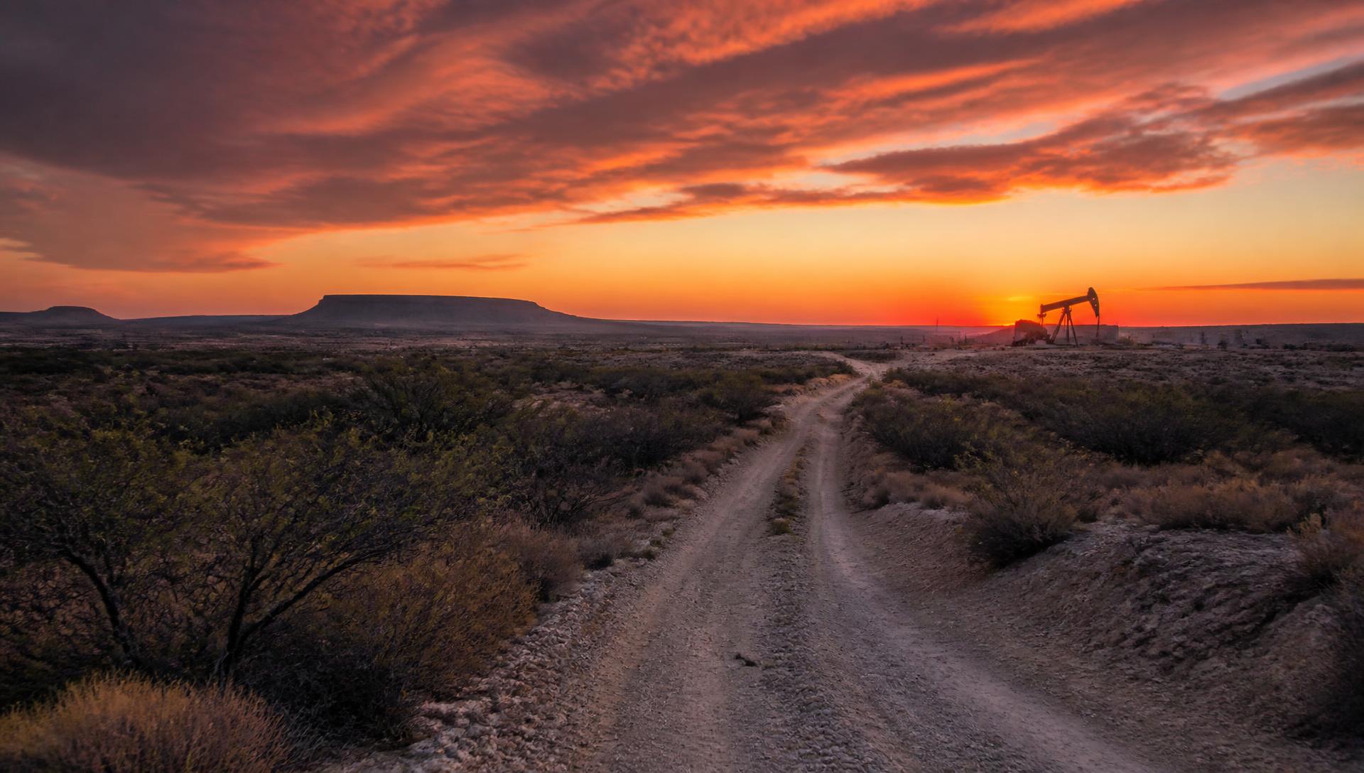 West Texas caliche road at dusk with a mesa and pumpjack on the horizon